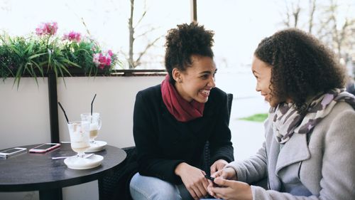 Free Two women smiling and chatting over a coffee at an outdoor cafe table. Stock Photo