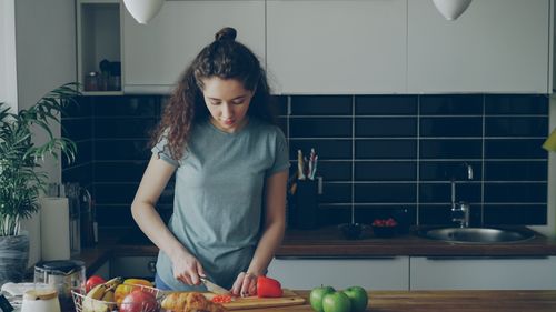 Free Young woman preparing food in a modern kitchen setting, cutting vegetables. Stock Photo