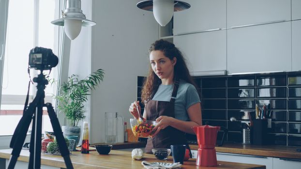 A woman records a cooking tutorial in her modern kitchen using a camera.