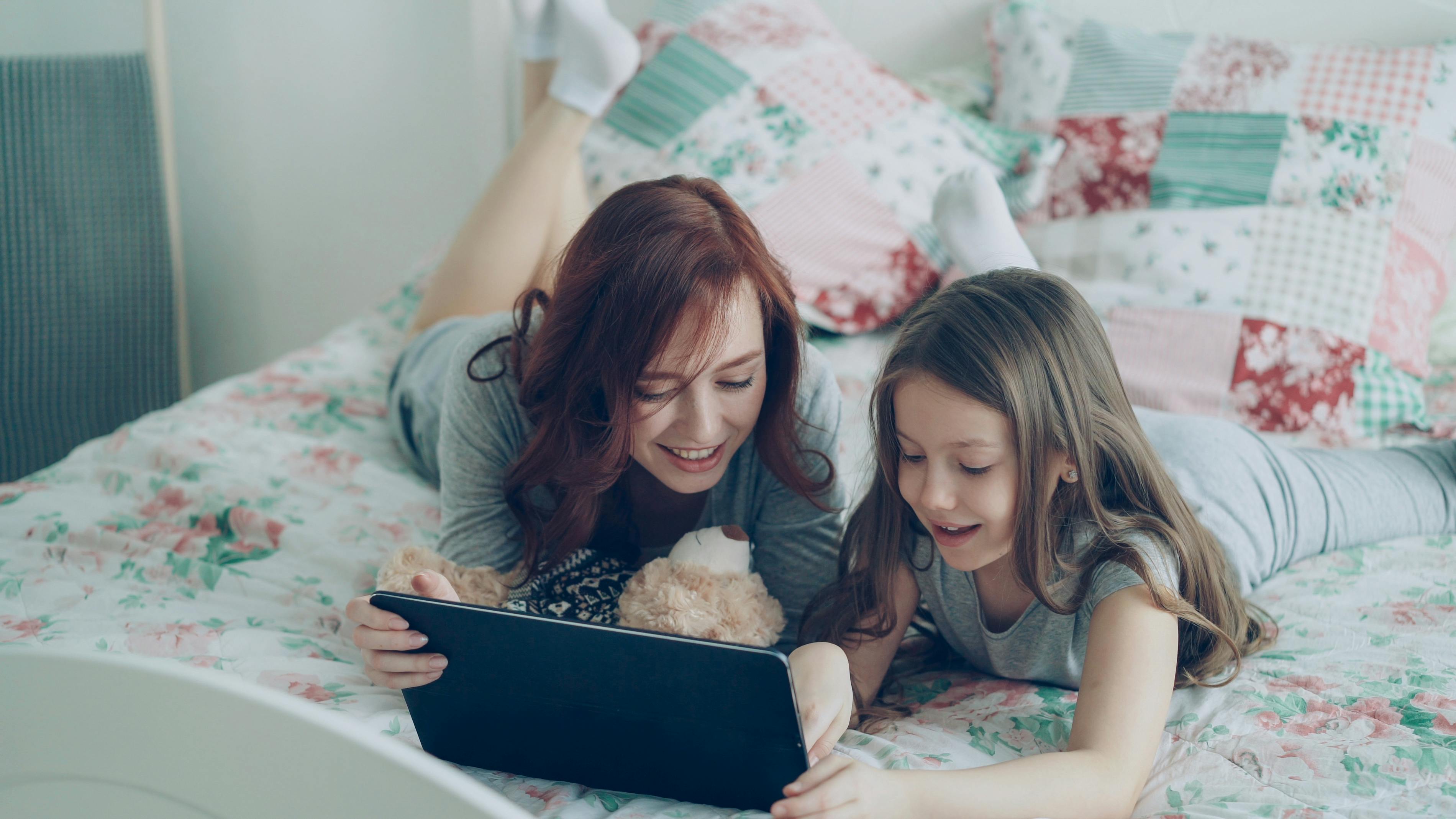 Mother and daughter having fun together on bed with a tablet in an indoor setting.