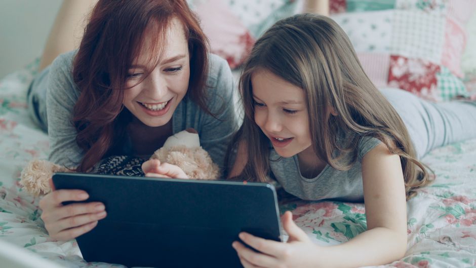 A mother and daughter enjoying time together while watching something on a tablet indoors.