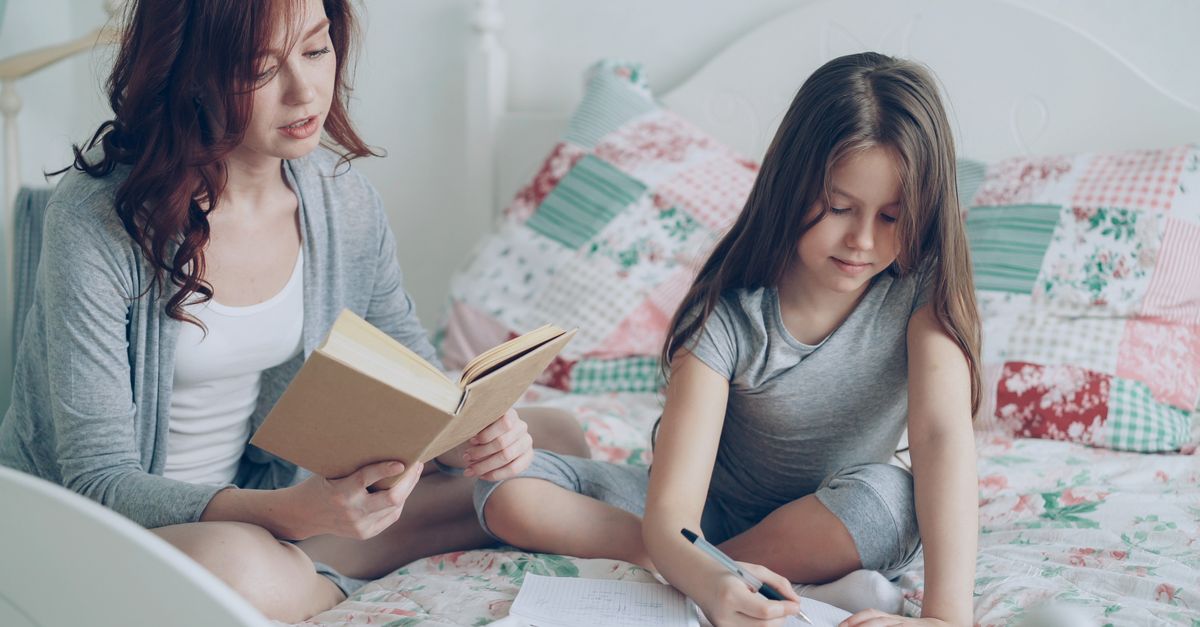 Mother and daughter bonding through reading and writing on a cozy bed.