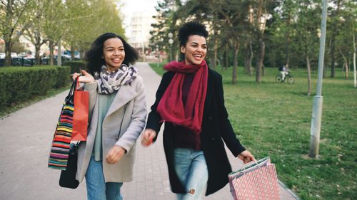 Free Two women enjoying a day of shopping outdoors on a park path, carrying colorful bags. Stock Photo