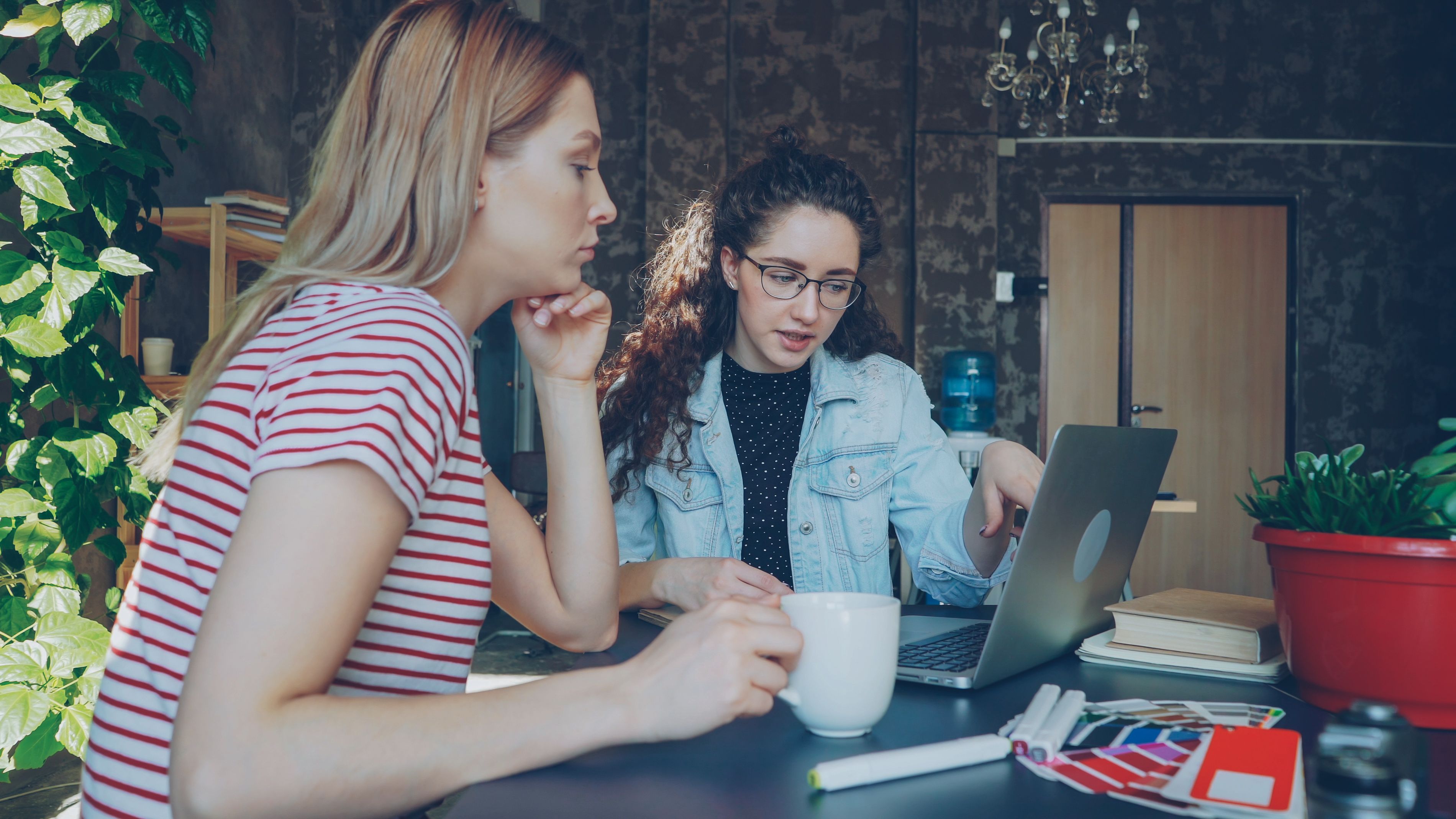 Two women in a modern office setting, collaborating on a laptop.