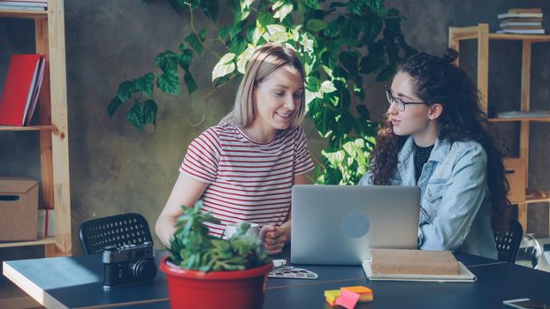 Two women discussing projects at a creative workspace desk.