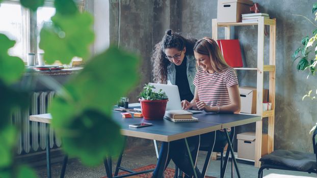 Two women collaborating on a laptop in a modern, plant-filled office.
