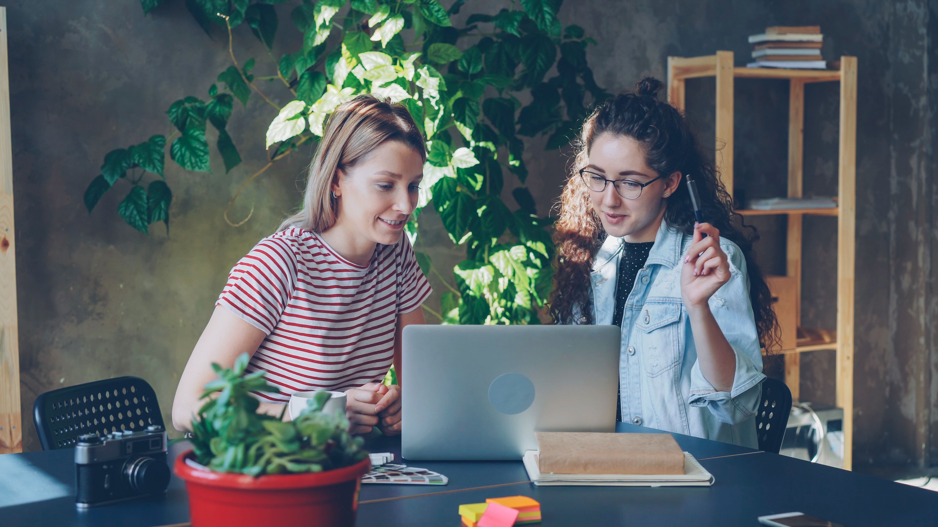 Abogado Familia en Chile — alimentos hijo mayor 18 | Two women work together on a laptop indoors, surrounded by plants.