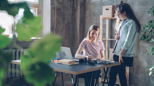 Free Two women working together at a desk in a modern, plant-filled office. Stock Photo