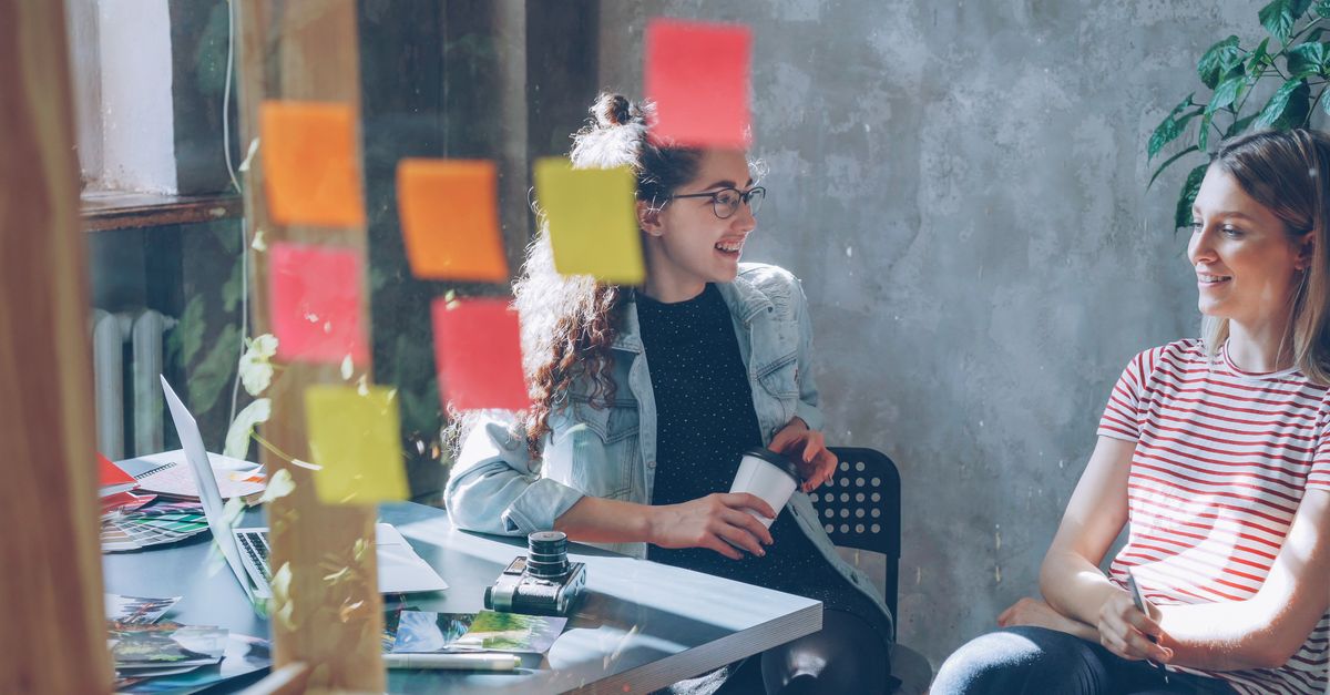 A person smiling while working on a laptop with a cup of tea, surrounded by sticky notes