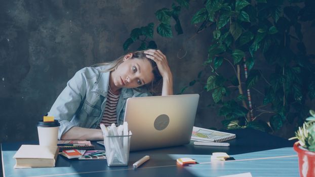 Woman in casual attire, deep in thought, working on laptop with coffee.