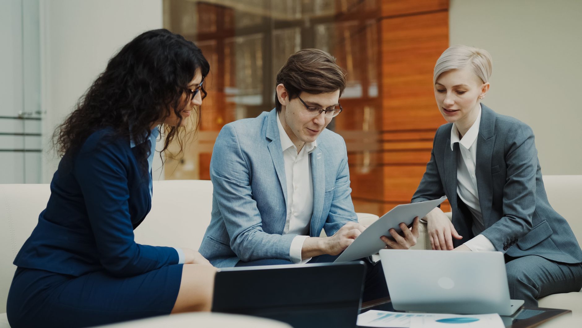 Three professionals engaged in a collaborative business meeting, using digital devices indoors.