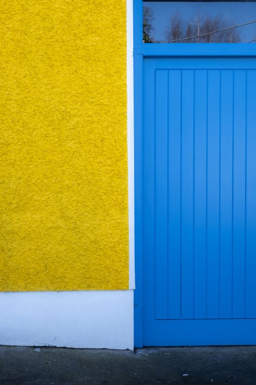 Free Colorful minimalist architecture with a bright yellow wall and blue door in Carlingford, Ireland. Stock Photo