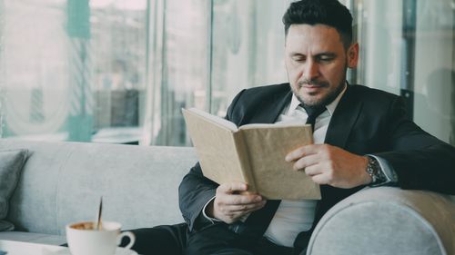 Free A businessman in a suit reads a book while relaxing in a cafe setting. Stock Photo