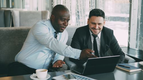 Free Two businessmen discussing work while using a laptop in a cafe setting. Stock Photo