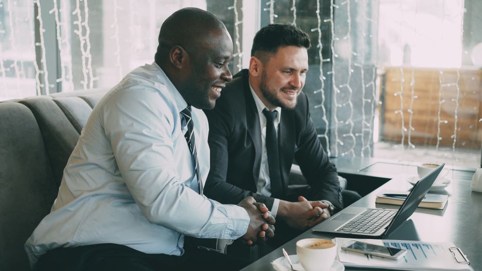 Two businessmen working together on a laptop in a cozy cafe setting. Two businessmen working together on a laptop in a cozy cafe setting.