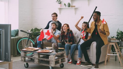 Free Group of diverse friends celebrating a sports victory indoors with Canadian flags. Stock Photo