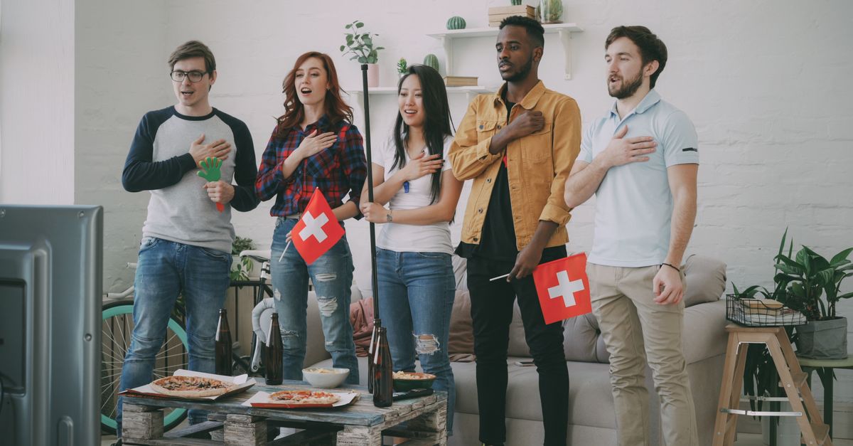 Friends watching TV at home, holding Swiss flags, showing excitement.
