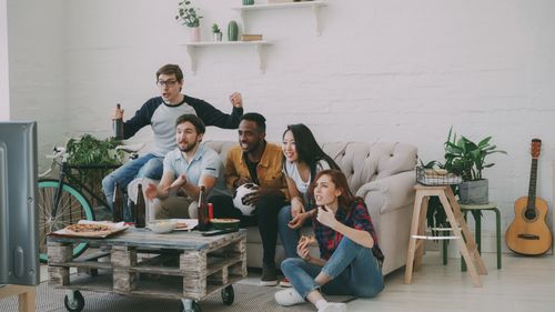 Free A diverse group of friends excitedly watching a sports game in a stylish living room. Stock Photo