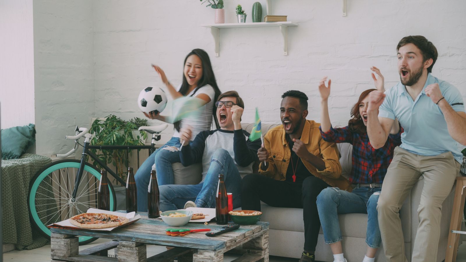 Friends in matching shirts celebrating a goal during a soccer watch party