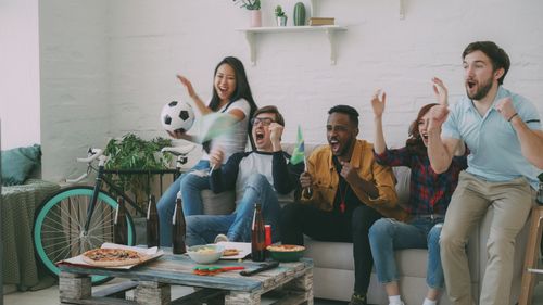 Free Enthusiastic friends celebrating a soccer game in a cozy living room setting. Stock Photo