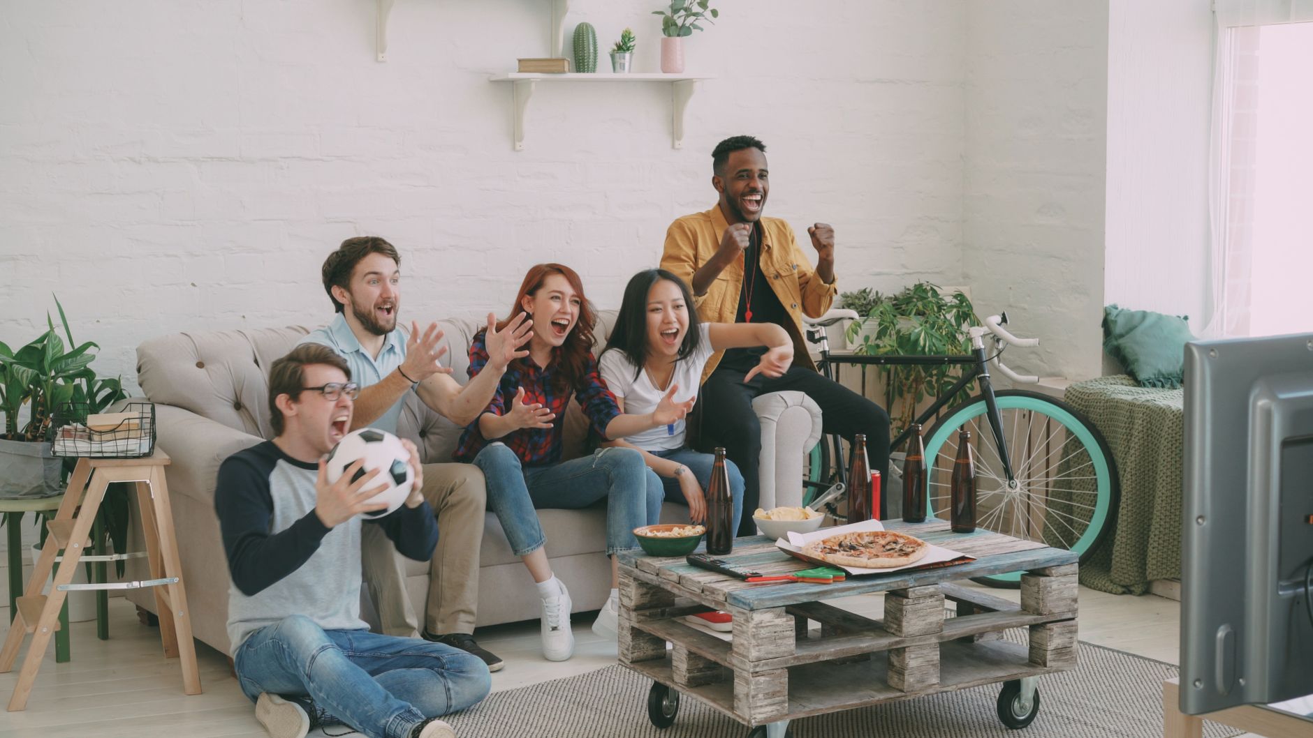 Group of friends watching soccer indoors, celebrating excitement.