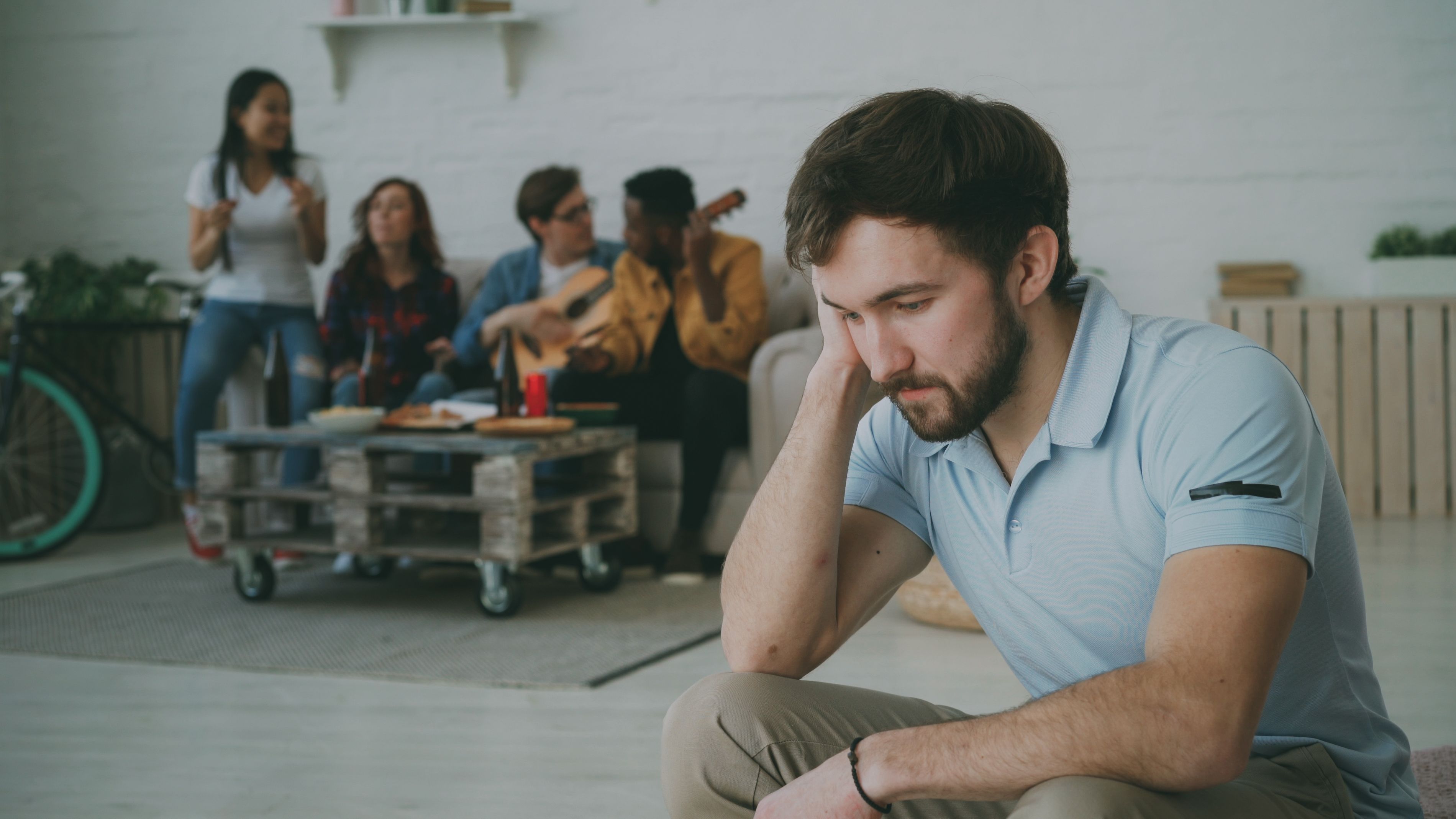 A young man sitting alone while others socialize in the background
