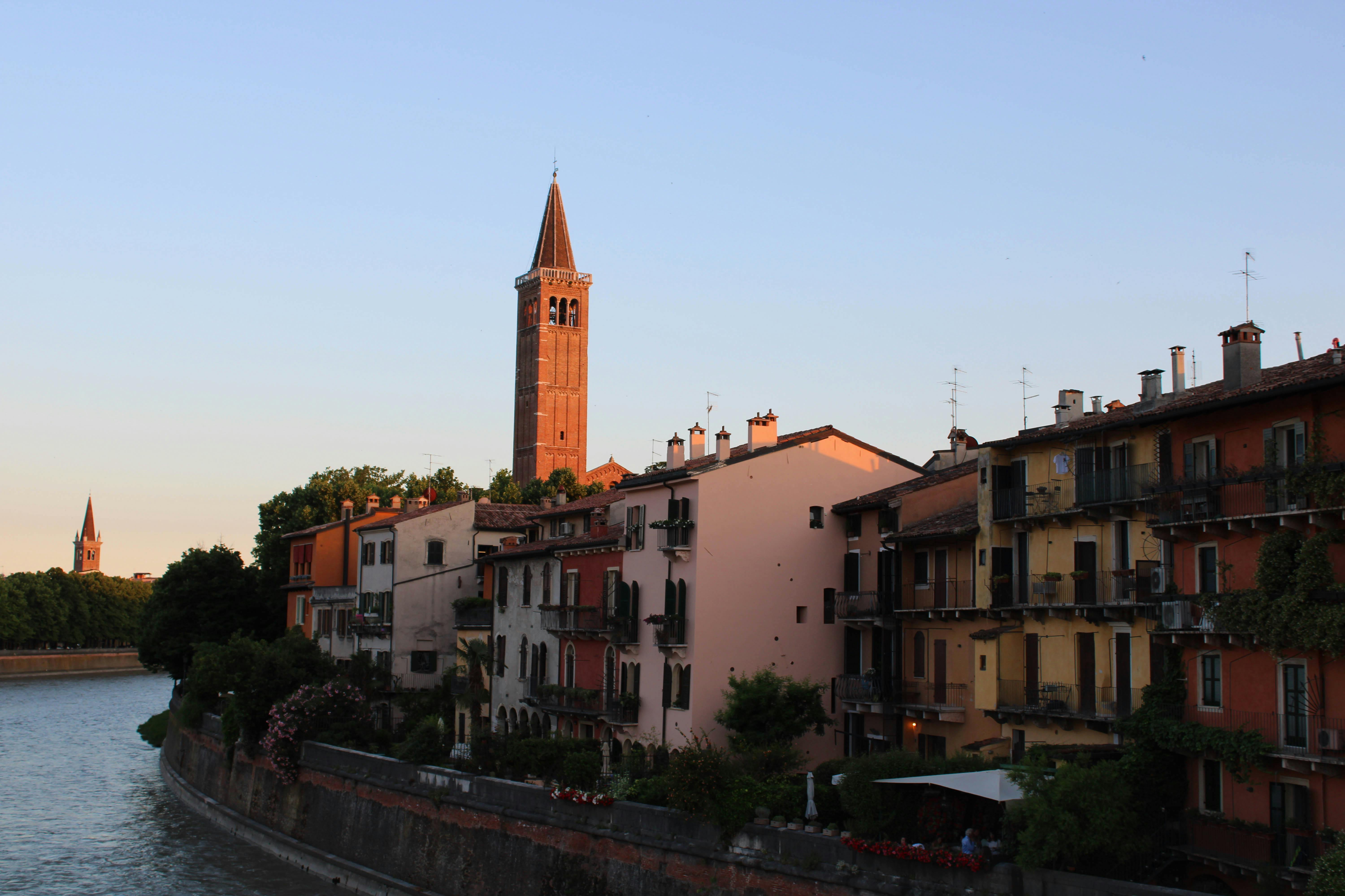 Charming view of Verona's colorful buildings and a bell tower by the river at sunset.