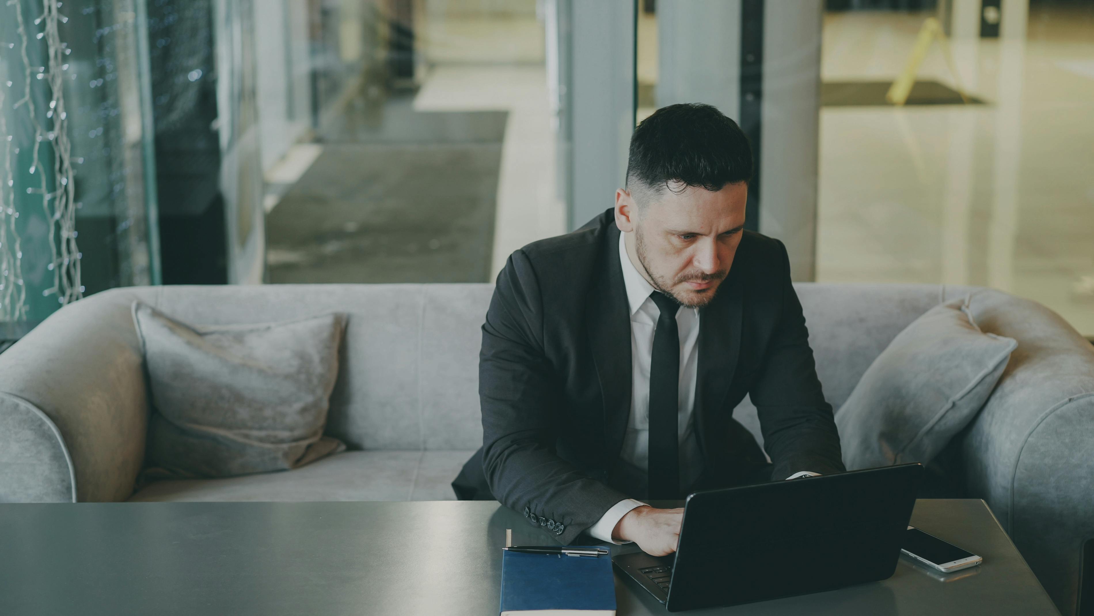 Businessman in suit focused on work at laptop in modern office lounge.