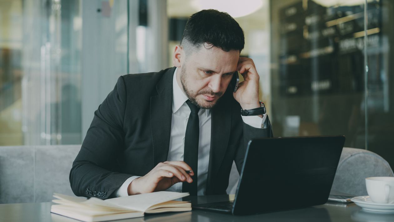 Homem de roupa social em um escritório, sentado diante do notebook e falando ao celular durante uma conversa de qualificação de lead