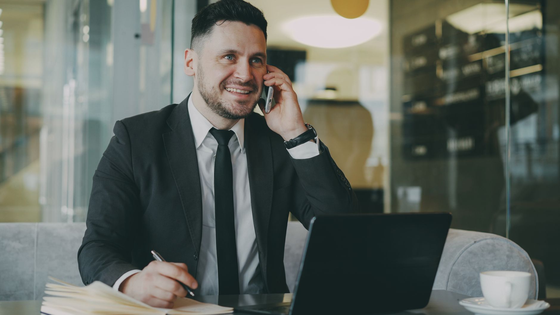 Professional man in a suit talking on the phone and working on a laptop indoors.