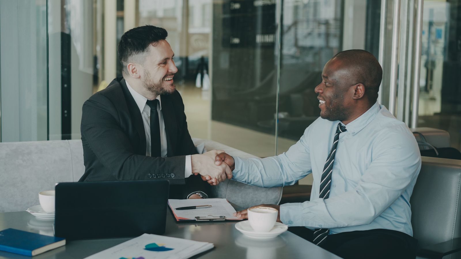 Two businessmen shaking hands over a deal at a modern office.