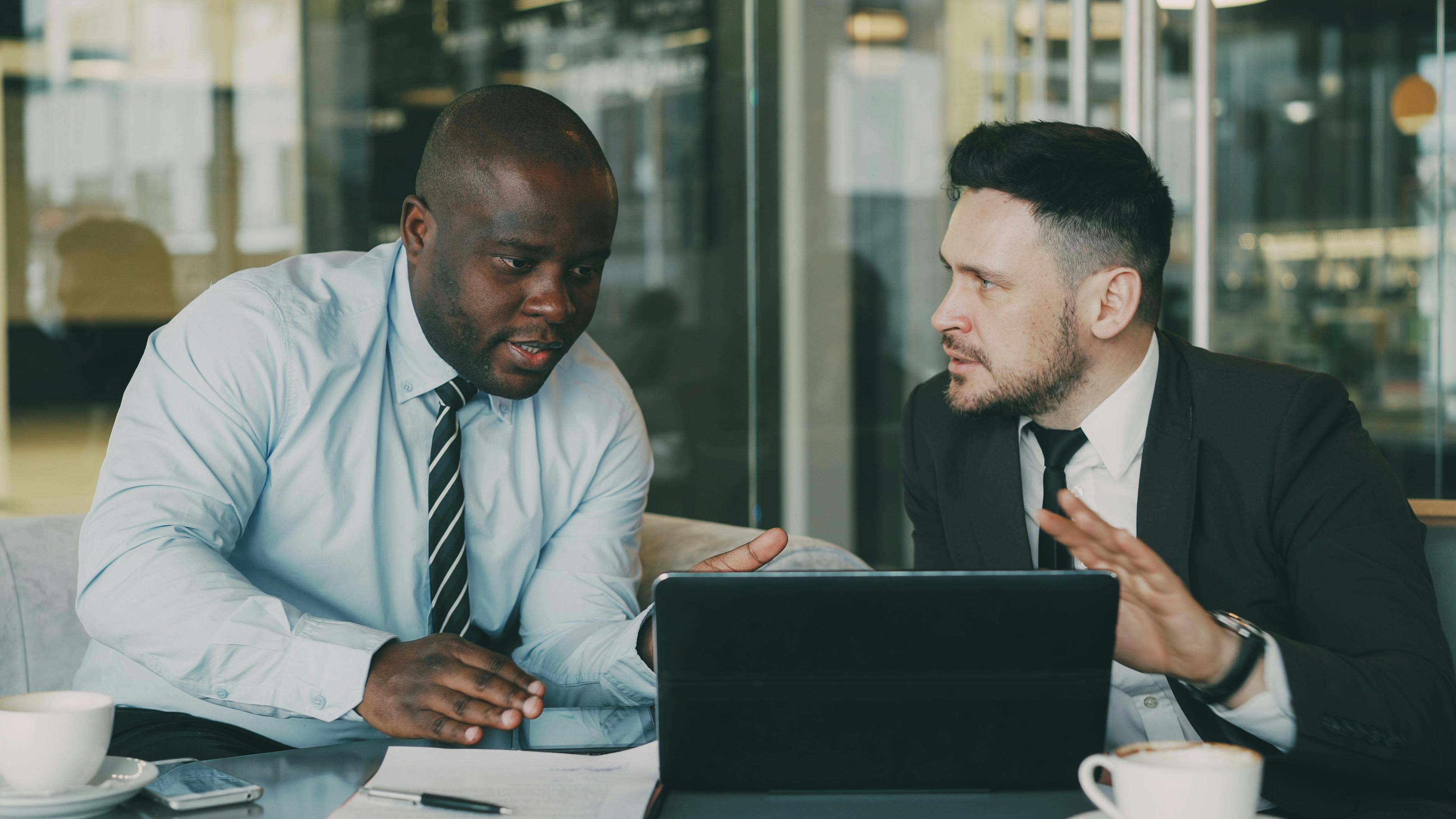 Inp buruk - Two professionals discussing business strategies with a laptop in an office environment.