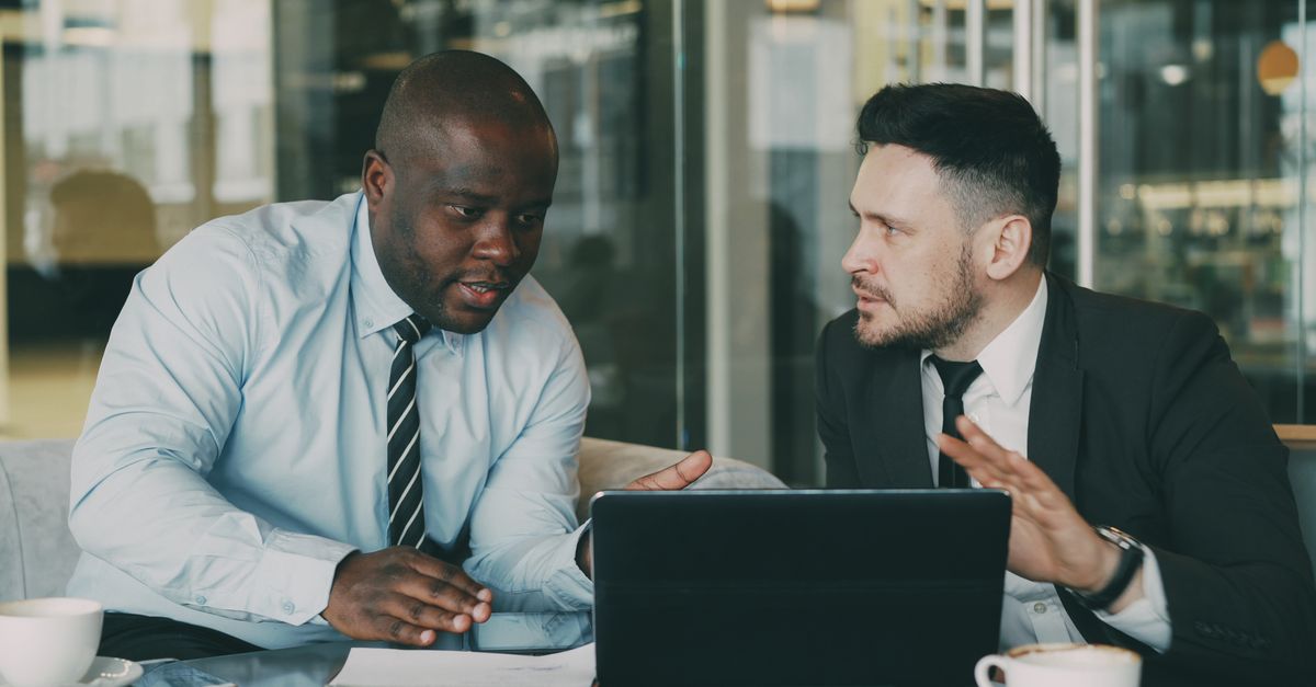 Two professionals discussing business strategies with a laptop in an office environment.