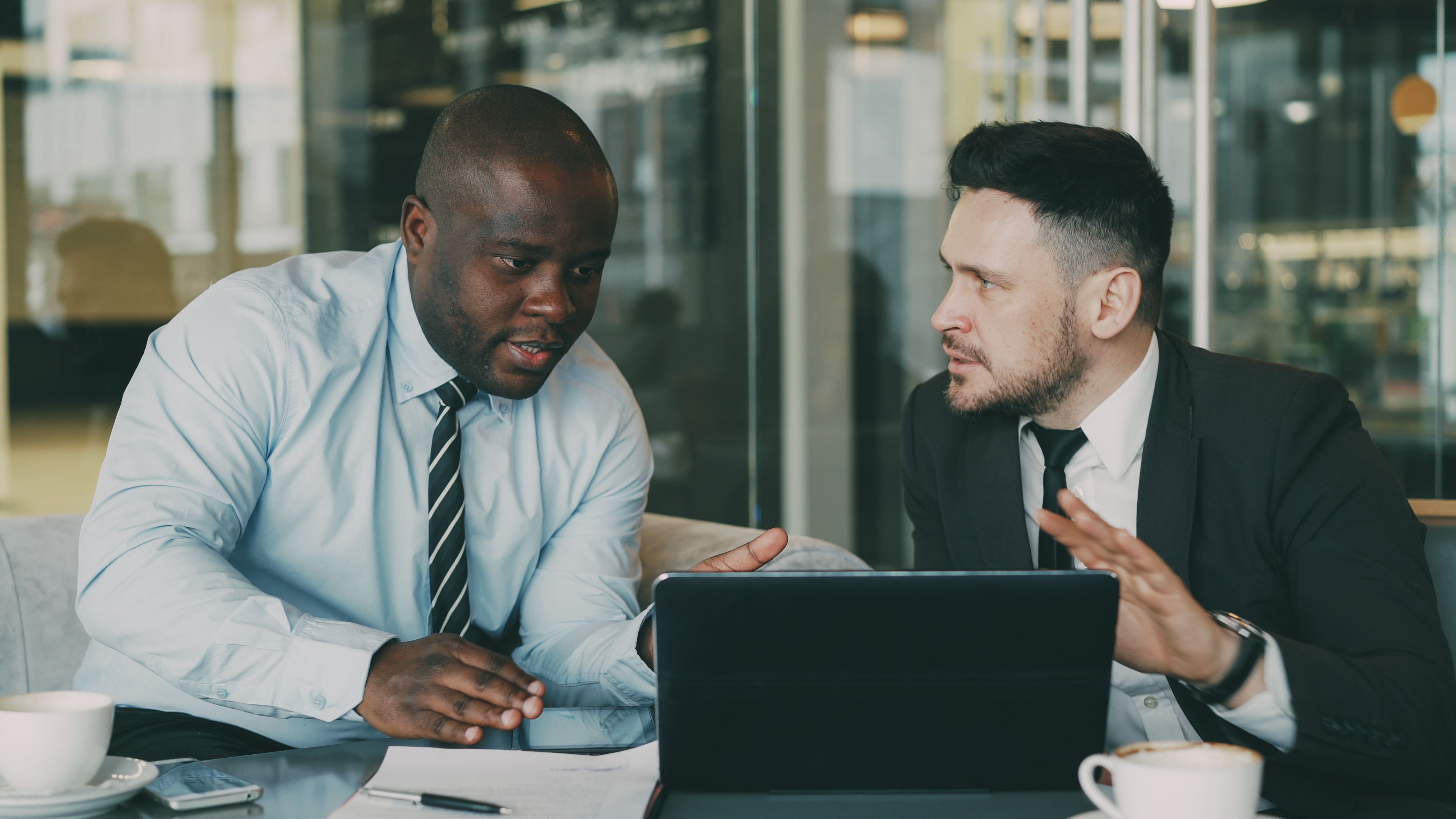 Alt Text: Two business professionals sitting side-by-side at a desk, reviewing data together on a laptop screen within a bright office space.
