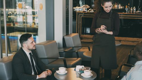 Free Casual business meeting at a modern café with two professionals and a waiter. Stock Photo