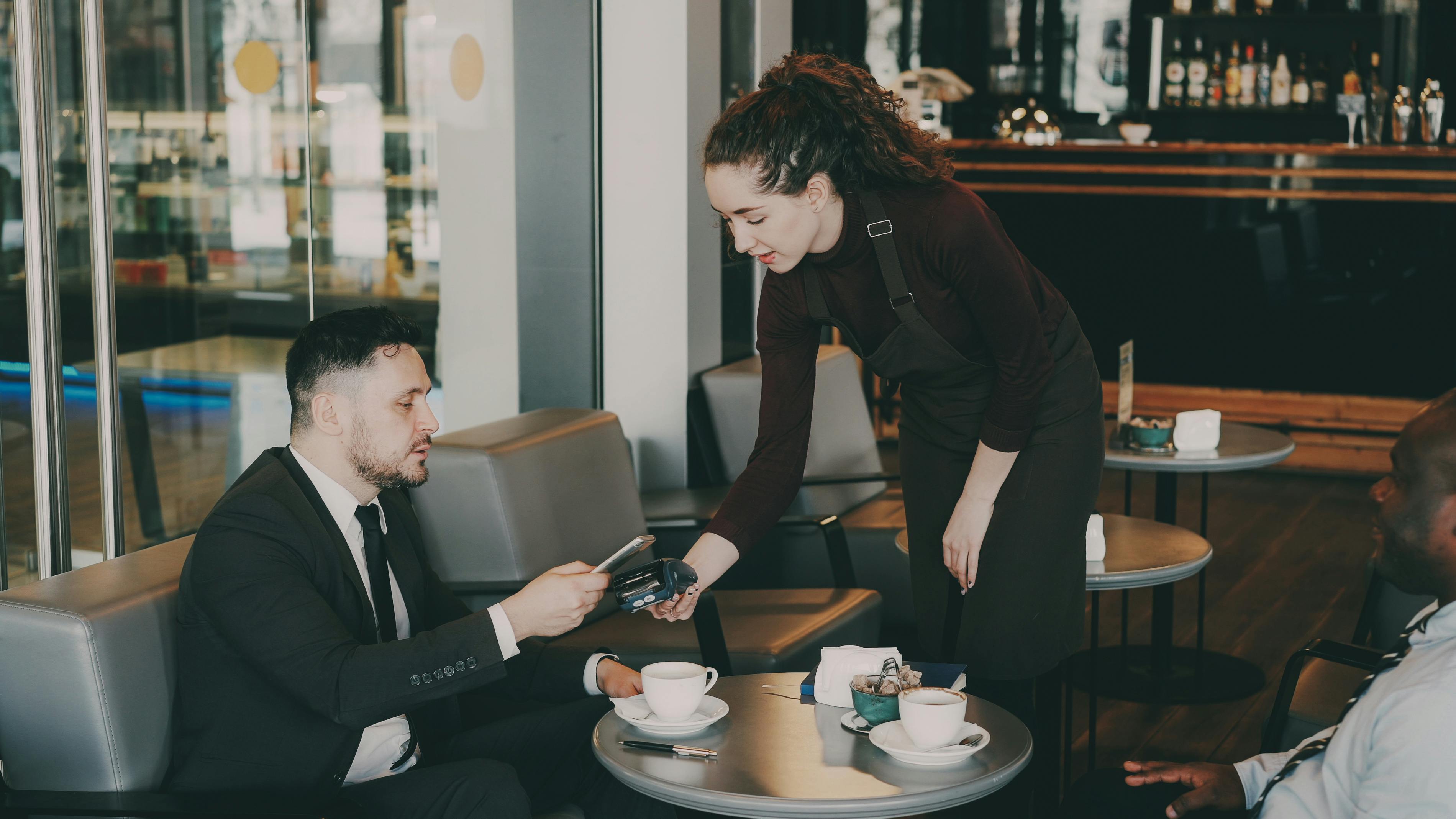 Business professionals in a café, paying with a card. Modern ambiance.