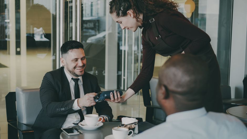 Professionals enjoying coffee in a stylish cafe, engaging in payment transaction.
