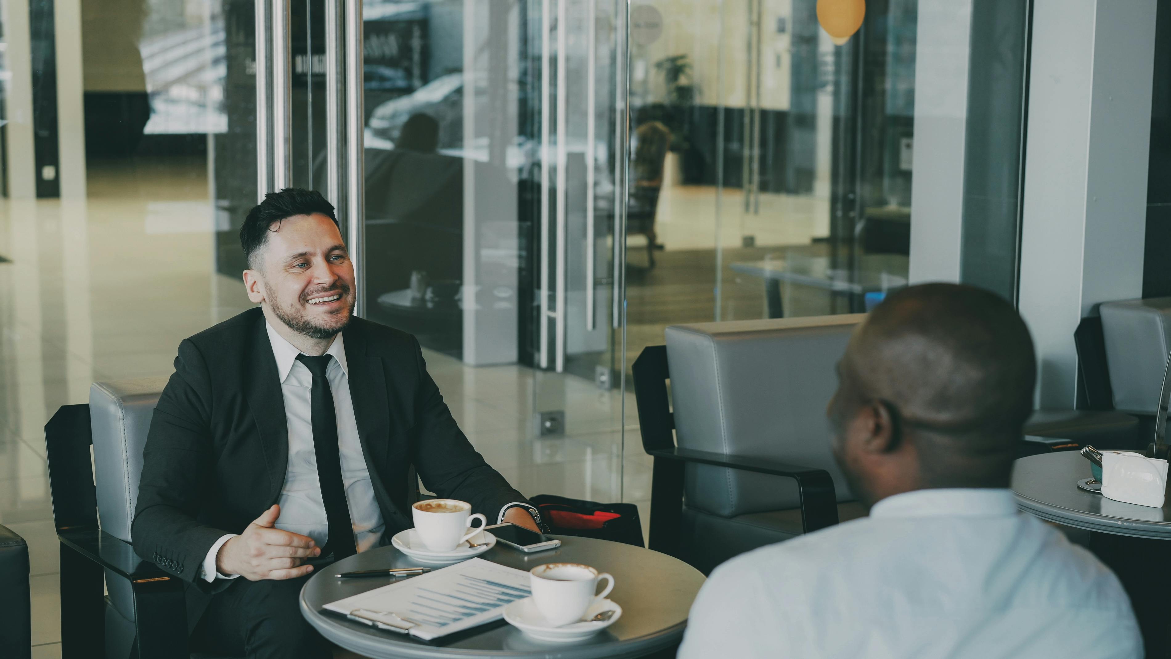 Two businessmen discuss plans over coffee in a modern indoor cafe setting.