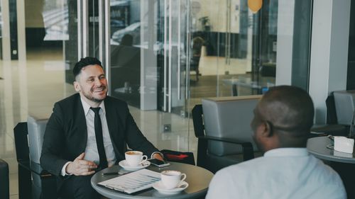 Free Two businessmen discuss plans over coffee in a modern indoor cafe setting. Stock Photo