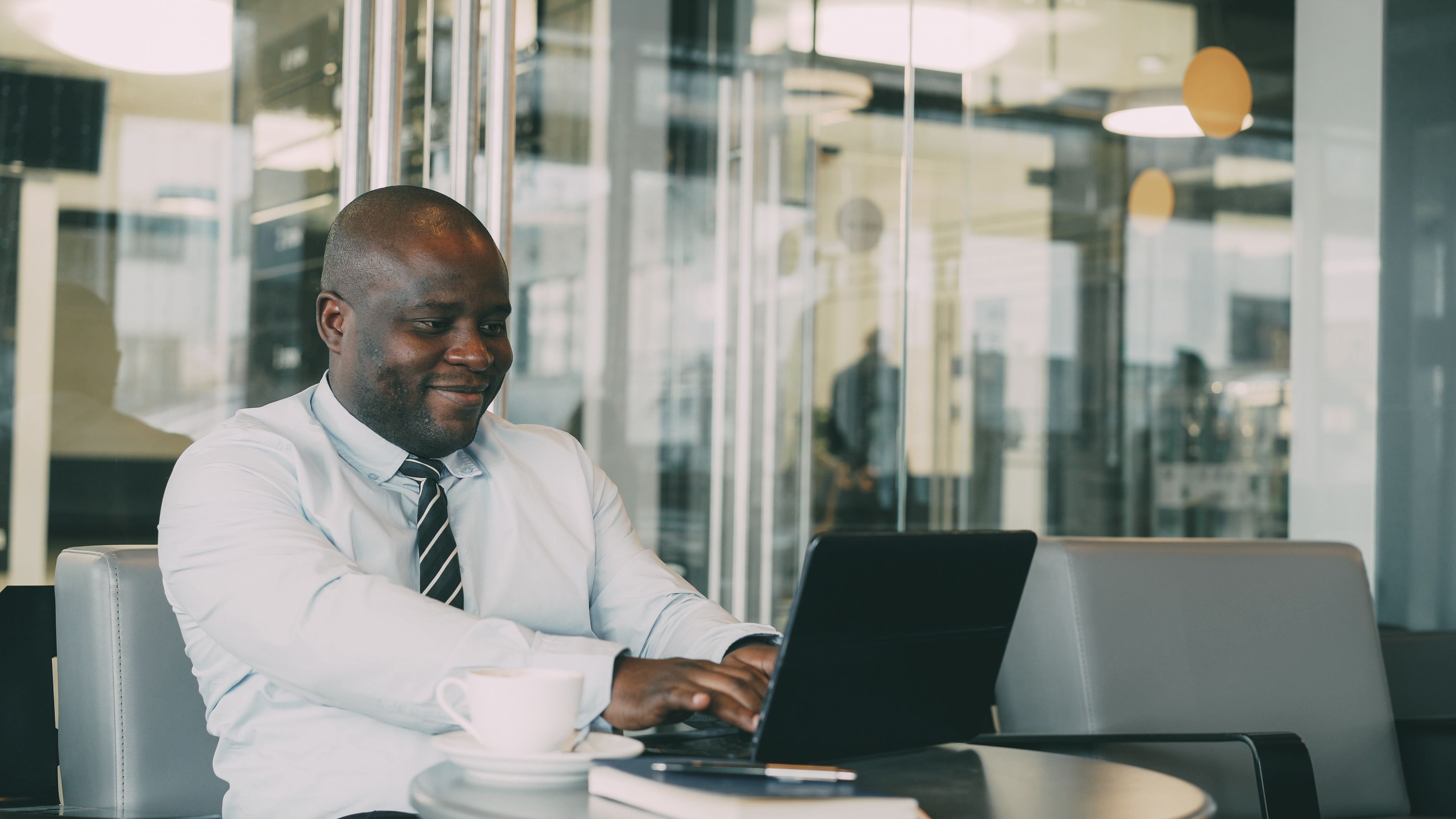 Smiling businessman using laptop at a cafe table with coffee.