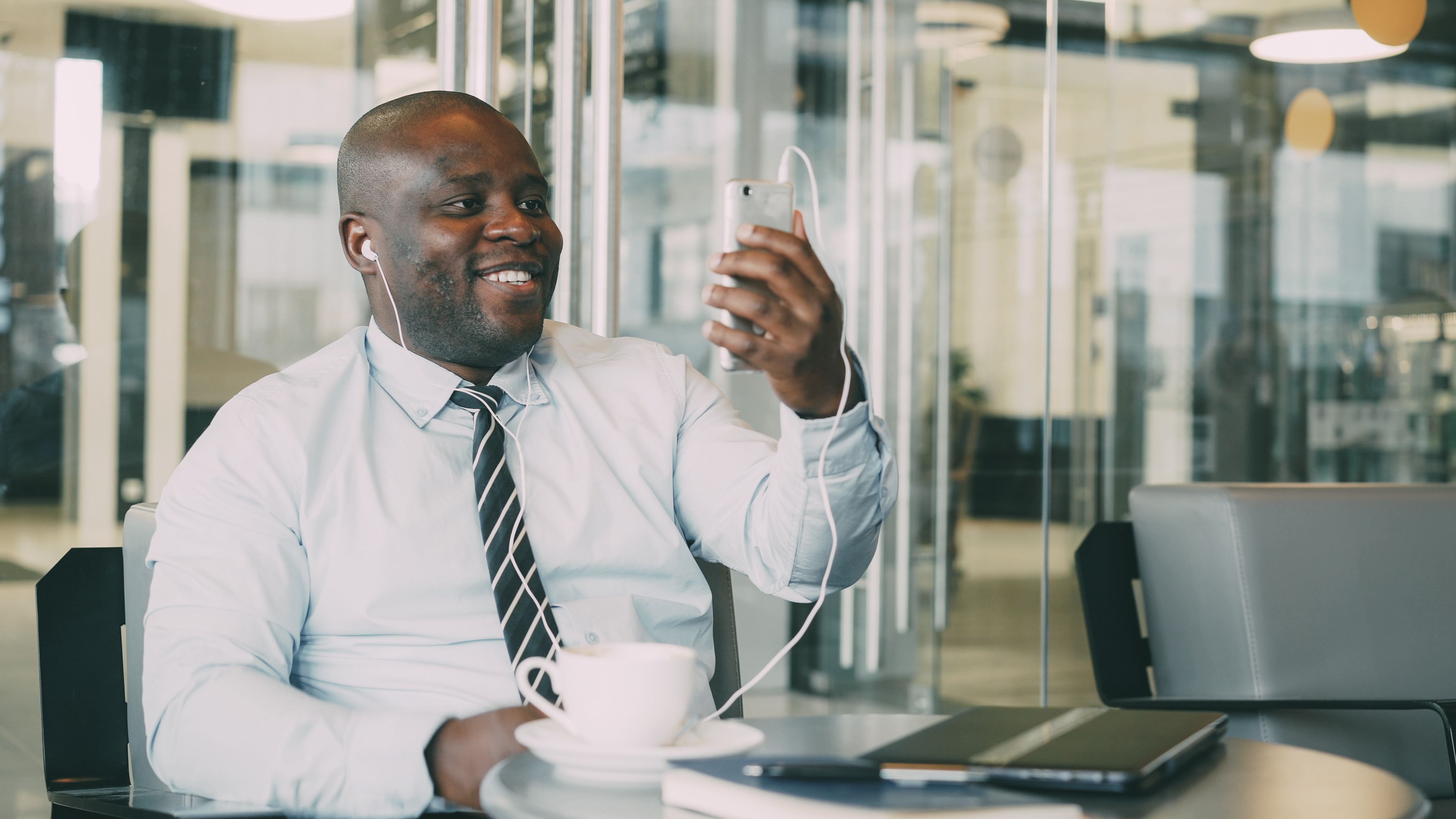 Smiling businessman in a modern office taking a video call with coffee and laptop.