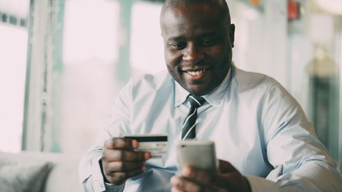Free A man in a tie uses his smartphone and credit card for online shopping indoors. Stock Photo