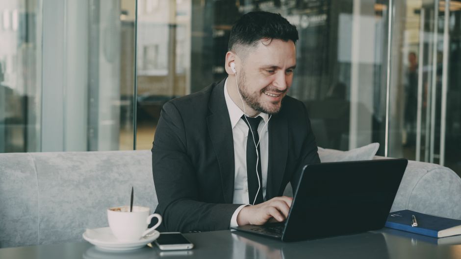 Why Internet Security Suites Alone Don’t Guarantee Total Privacy Businessman in a suit using a laptop in a cafe, enjoying coffee and listening to headphones.