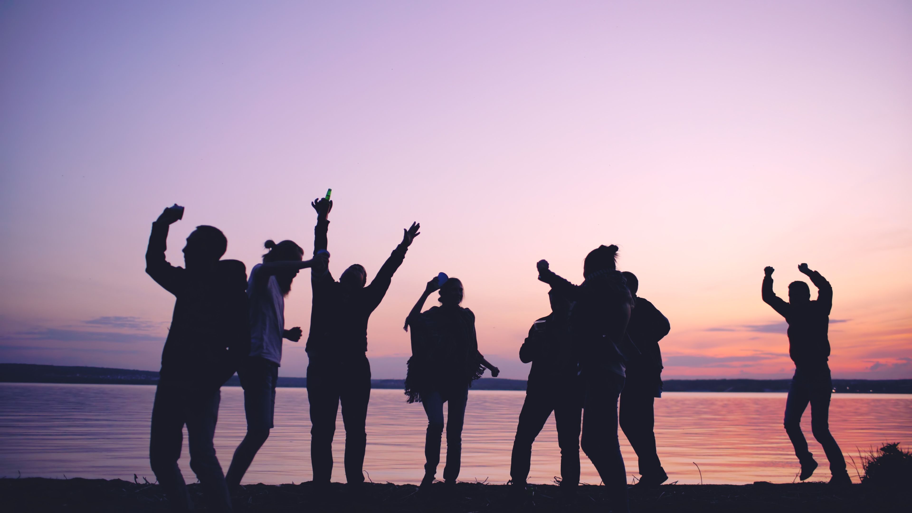 Group of young adults celebrating by a lake during a vibrant sunset.