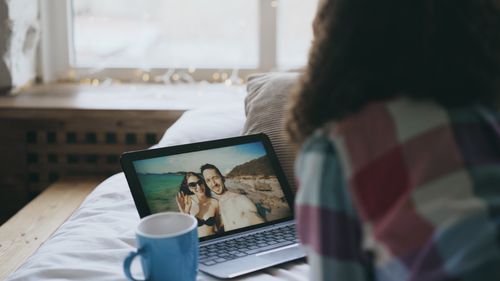 Free A person looking at a beach vacation photo on a laptop indoors with a mug. Stock Photo