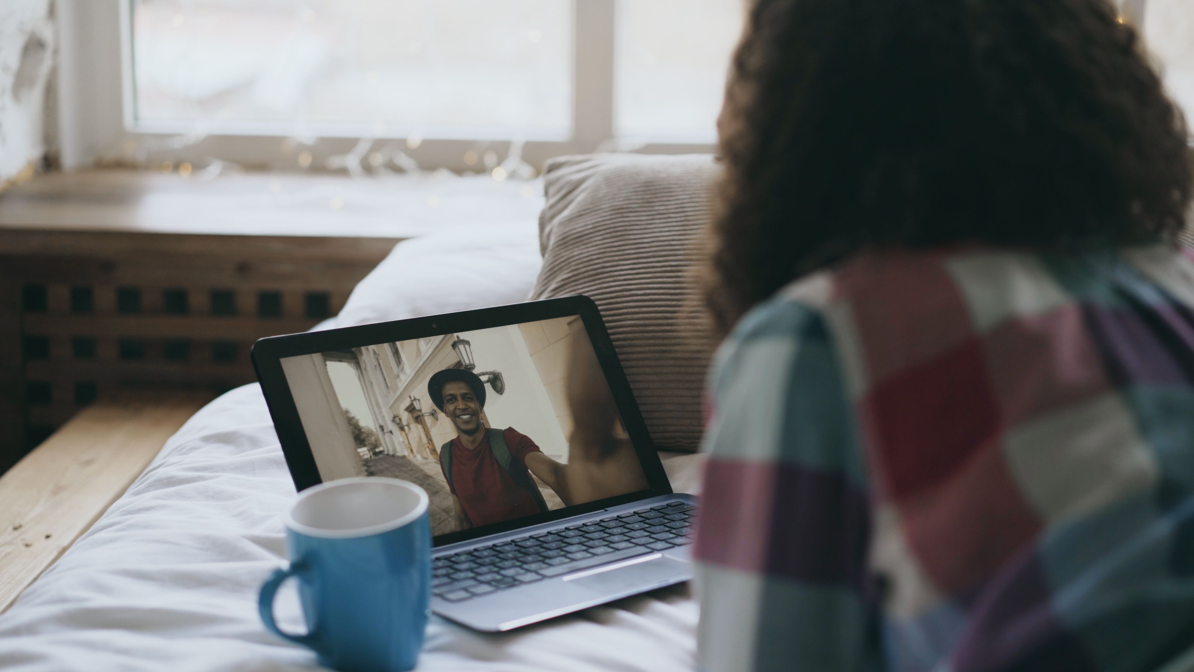 Woman enjoys a video call on a laptop in a cozy, well-lit room with a mug nearby.