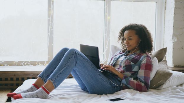 Young woman enjoying a relaxing day at home using a laptop, surrounded by soft decor.