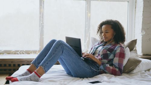 Free Young woman enjoying a relaxing day at home using a laptop, surrounded by soft decor. Stock Photo