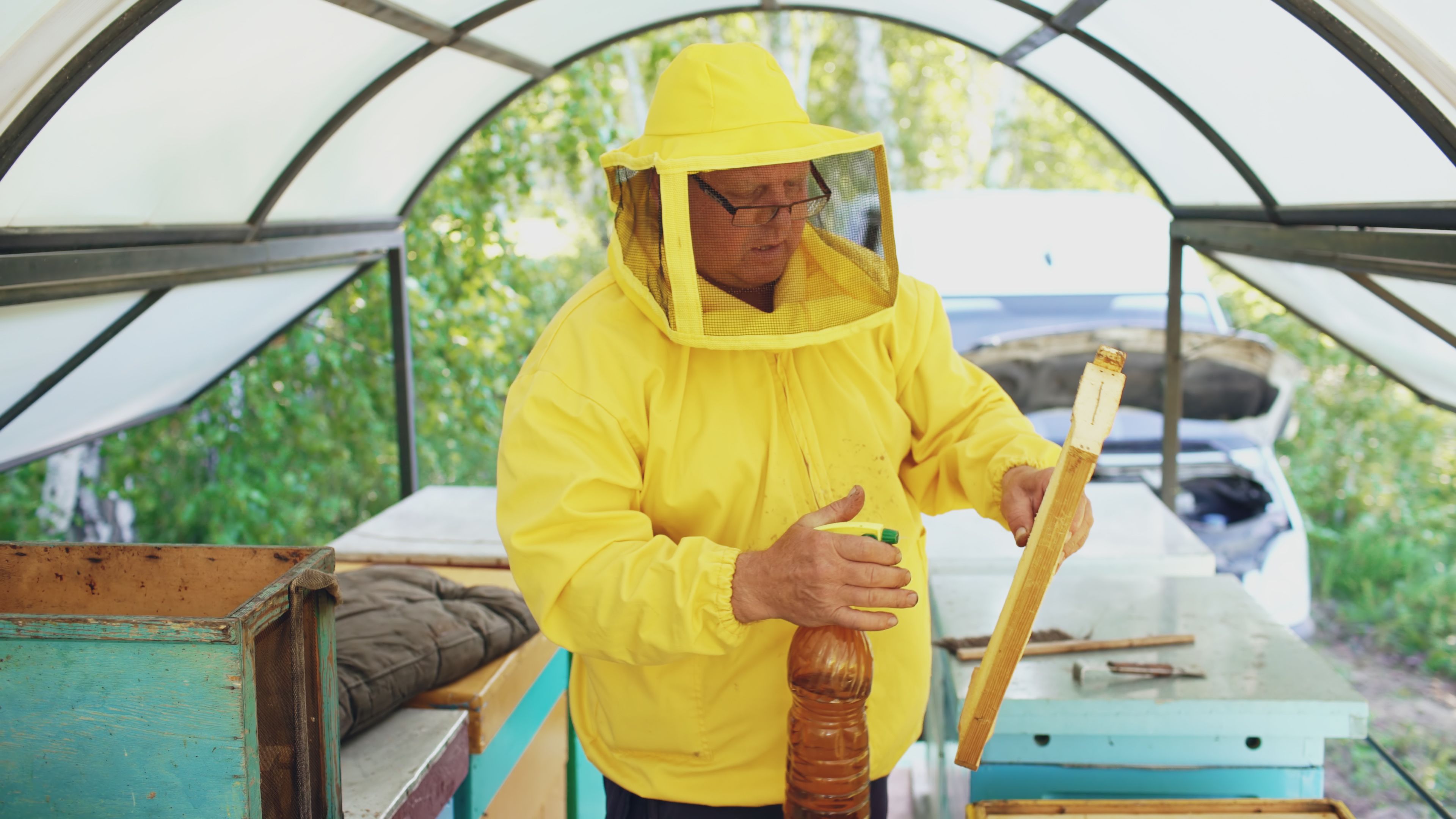 Beekeeper working in protective gear with honeycombs in a sheltered area.