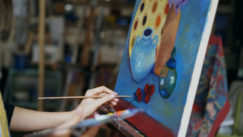 Como a Arte Pode Transformar seu Bem-Estar Emocional 2 Close up of artist's hand painting a still life on canvas in a studio environment.